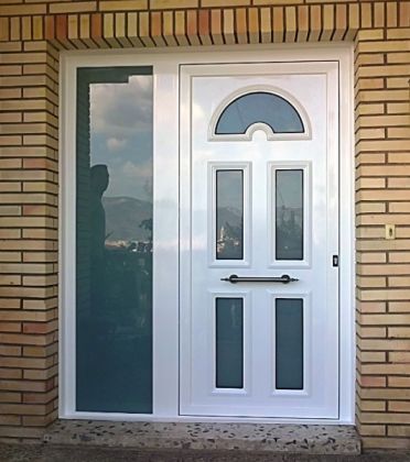 Puerta de aluminio para entrada de vivienda con panel decorativo y fijo lateral con vidrio